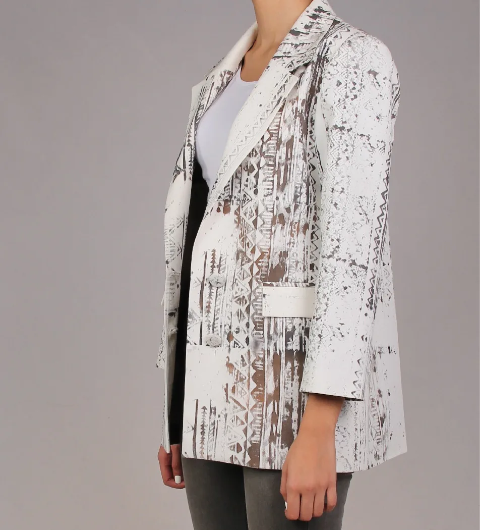 A woman in a white tailored blazer painted with charcoal and taupe zigzags, triangles and speckles, seen from the side.