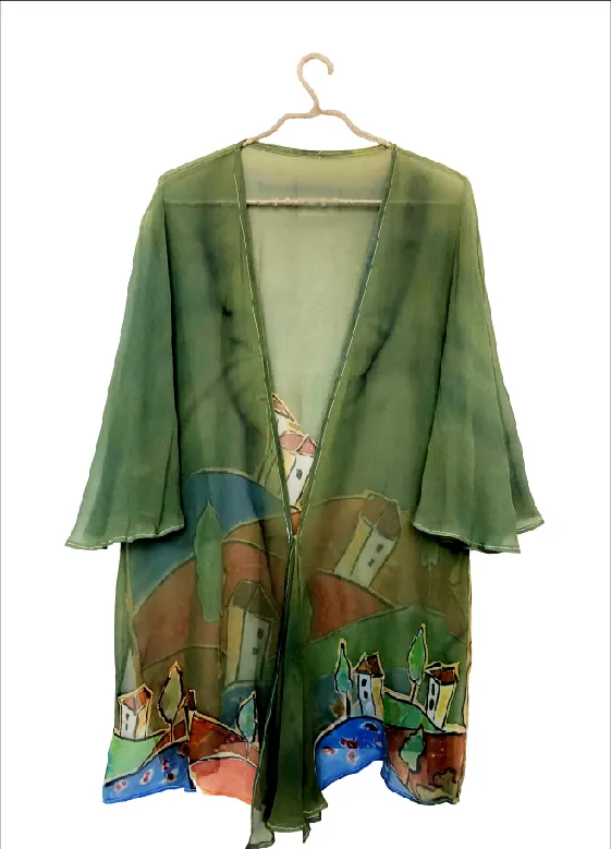 A sheer olive-green kimono on a hanger, painted along the hem with small houses, trees and a blue stream.