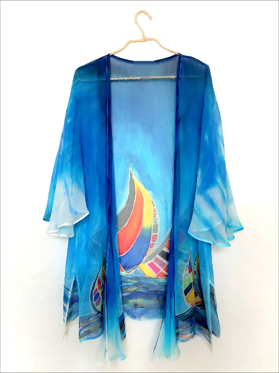 A sheer blue kimono on a hanger, painted with a large sailboat in red, yellow, blue and gray and smaller boats on the waves along the hem.