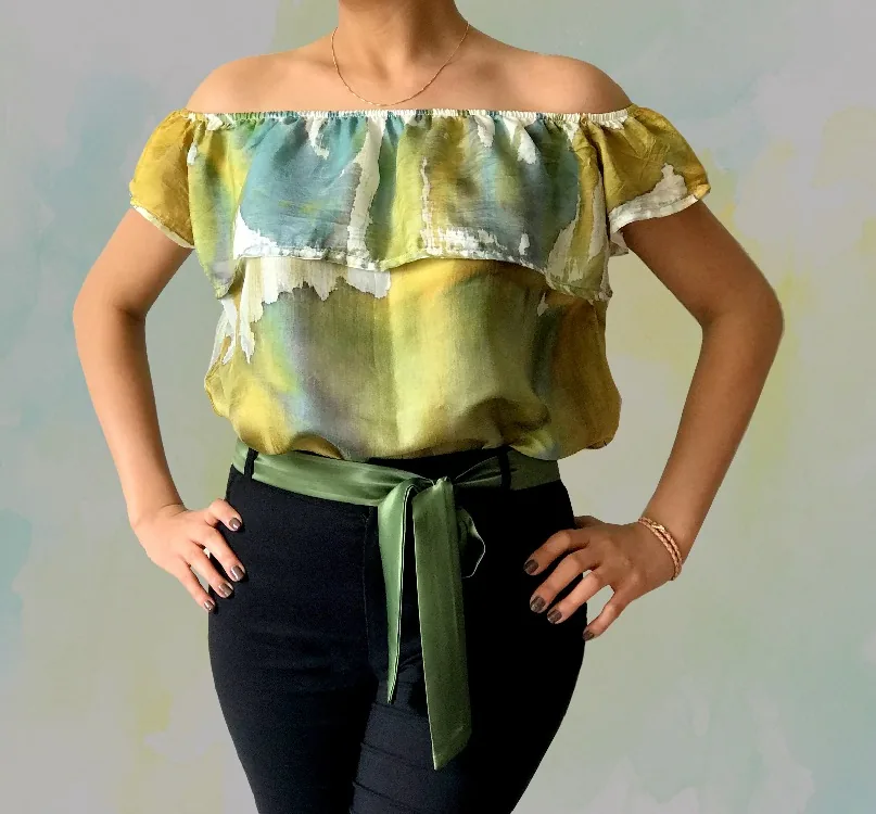 An off-shoulder ruffled top painted in ochre, pale green and sky blue with white highlights, worn with a green satin sash.